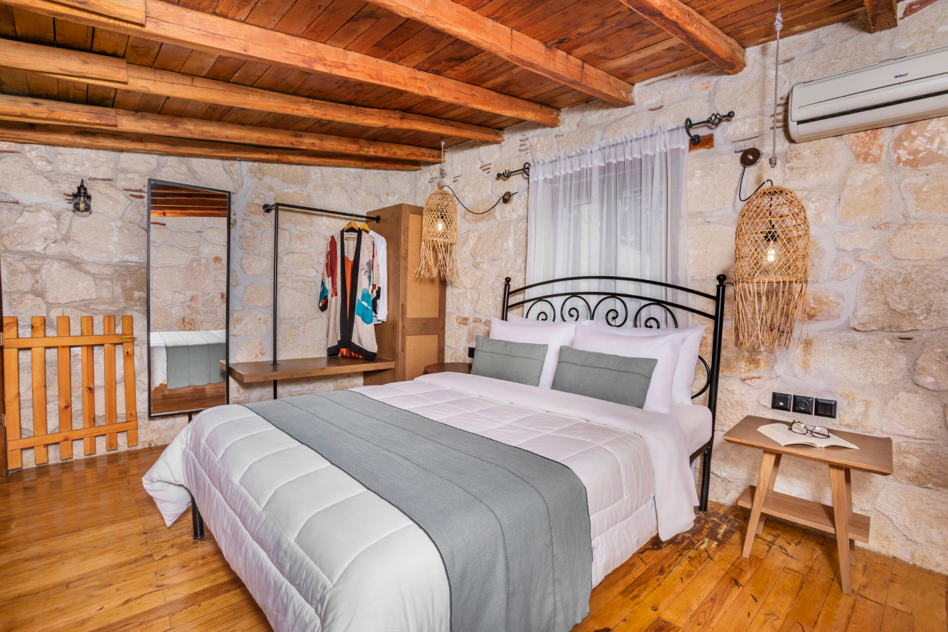 Bedroom with iron bed, stone walls and timber ceiling.