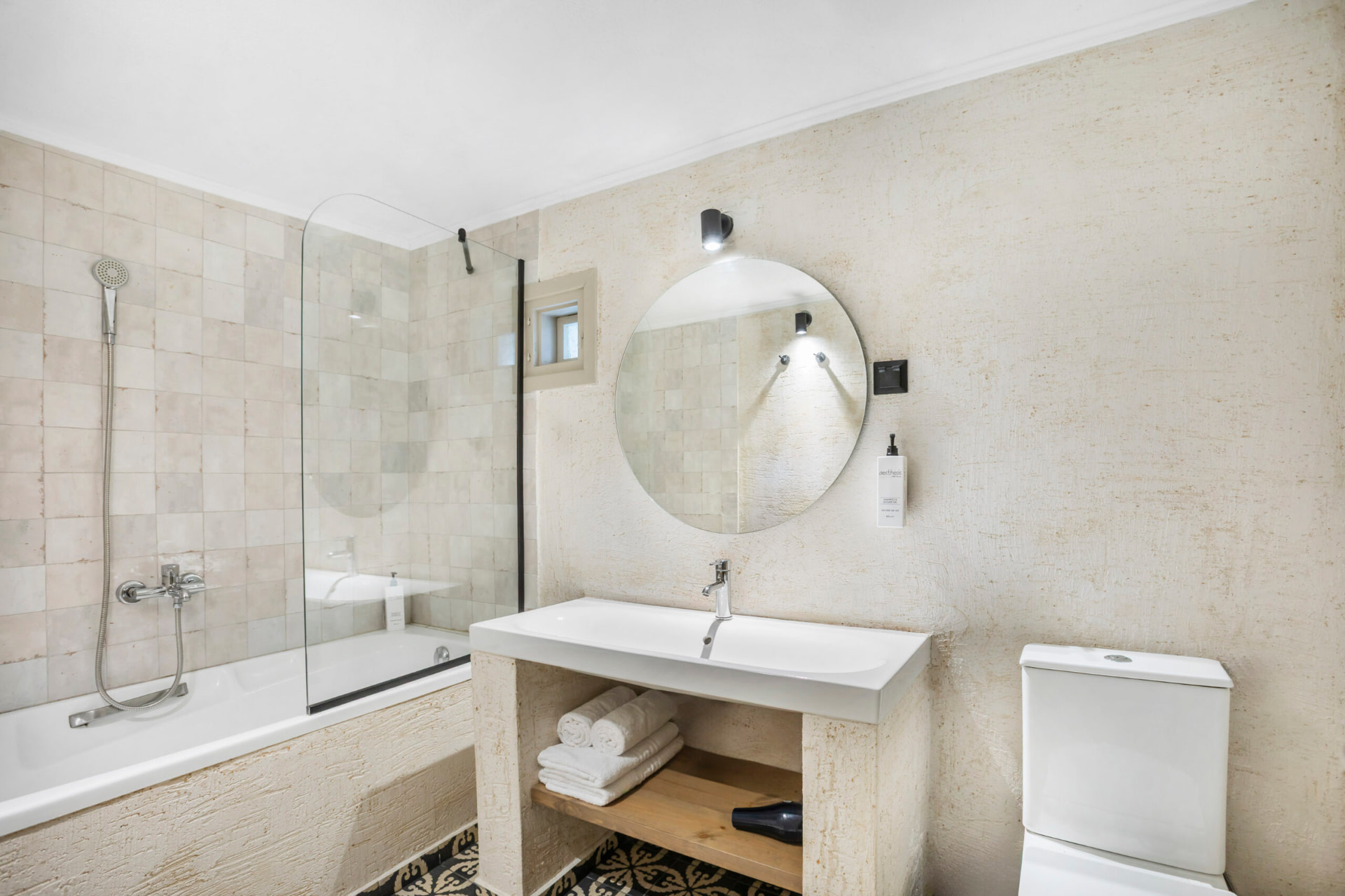 Bathroom with round mirror, bathtub and mosaic floor.