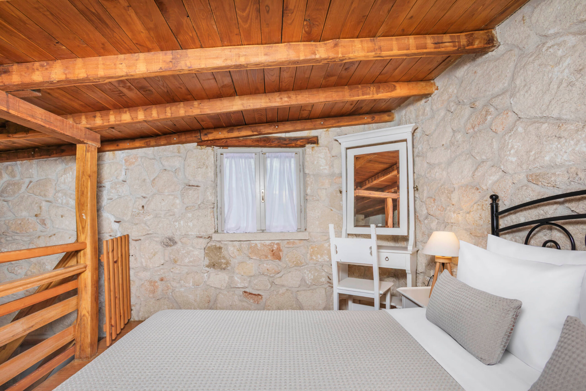 Loft bedroom under the wooden roof with stone walls.
